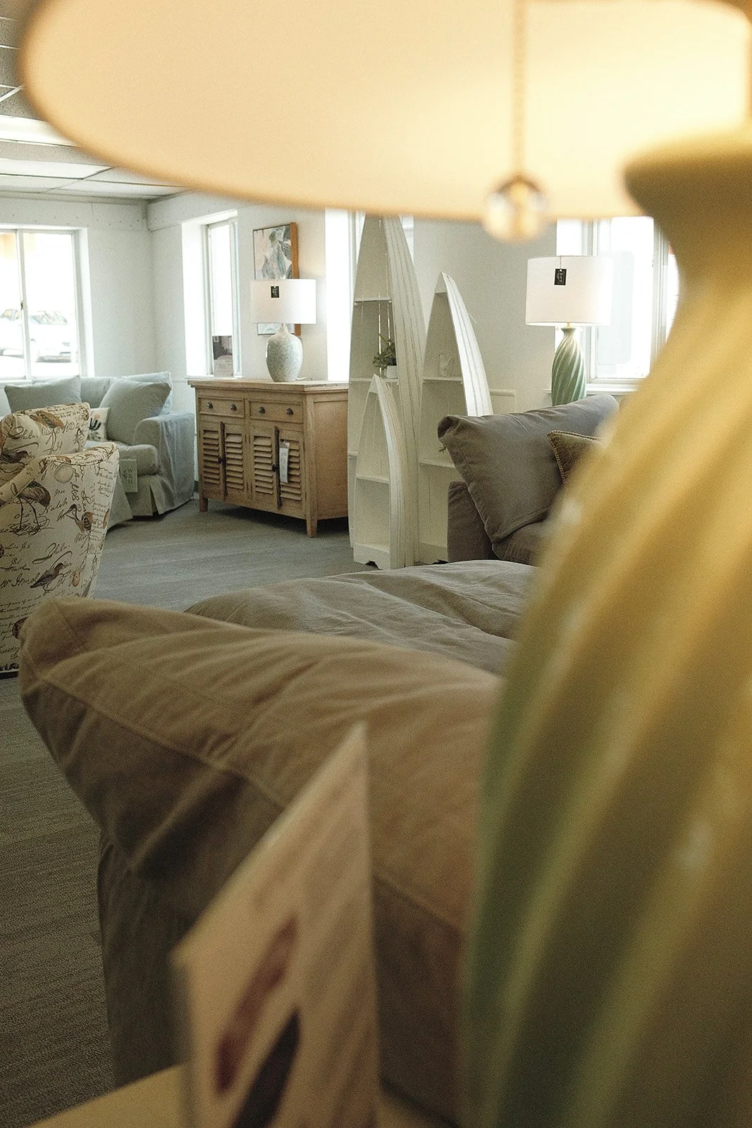 View of a cozy living room with multiple sofas, lamps, a wooden cabinet, and decorative bookshelves, seen through a partially obstructed view from a bed or similar furniture.
