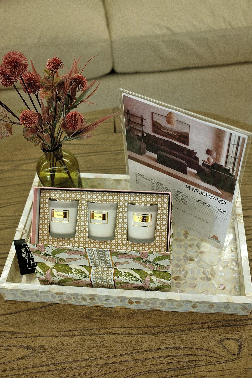 Decorative tray with flower vase, candle set, and interior decor brochure on a wooden table.
