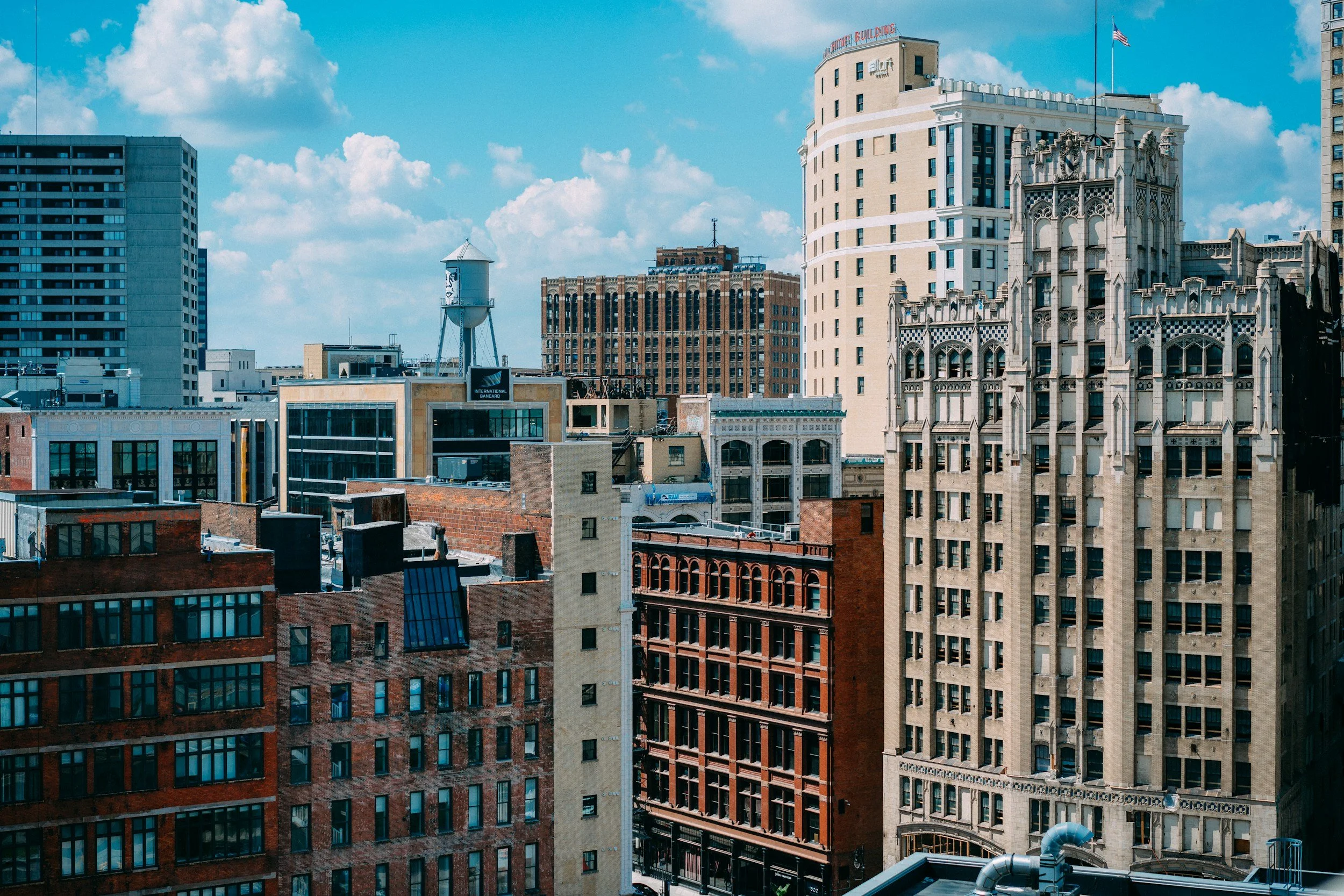 City skyline with various architectural styles and a water tower under a blue sky with clouds