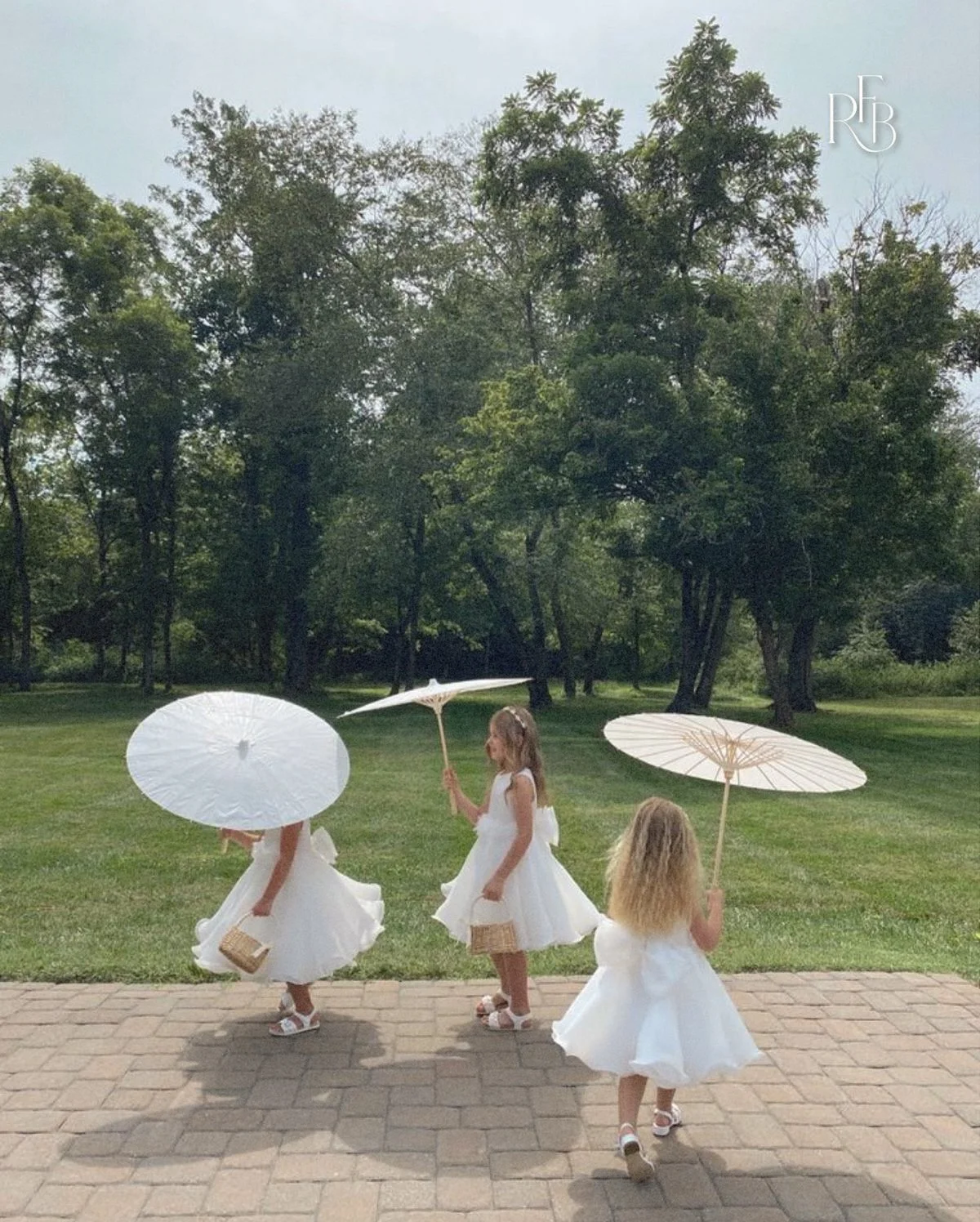 Young girls dressed for a wedding walking together with parasols at an outdoor venue