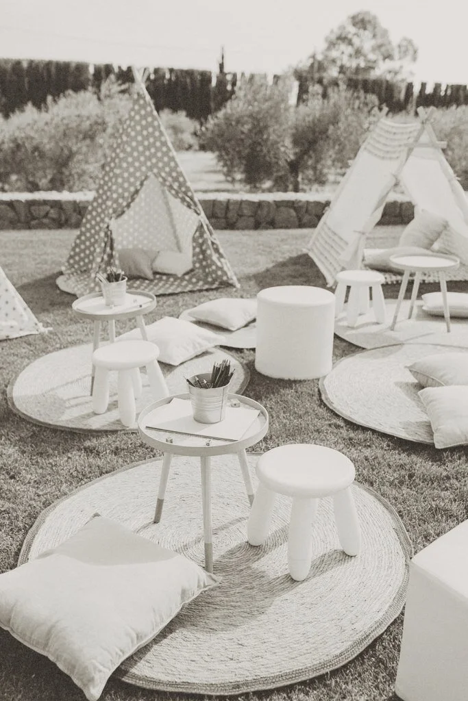 Curated wedding childcare play area with teepees, rugs, and soft seating outdoors