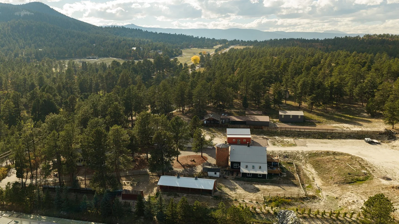 Aerial view of a rural landscape with scattered houses, trees, and dirt roads surrounded by mountains in the distance.