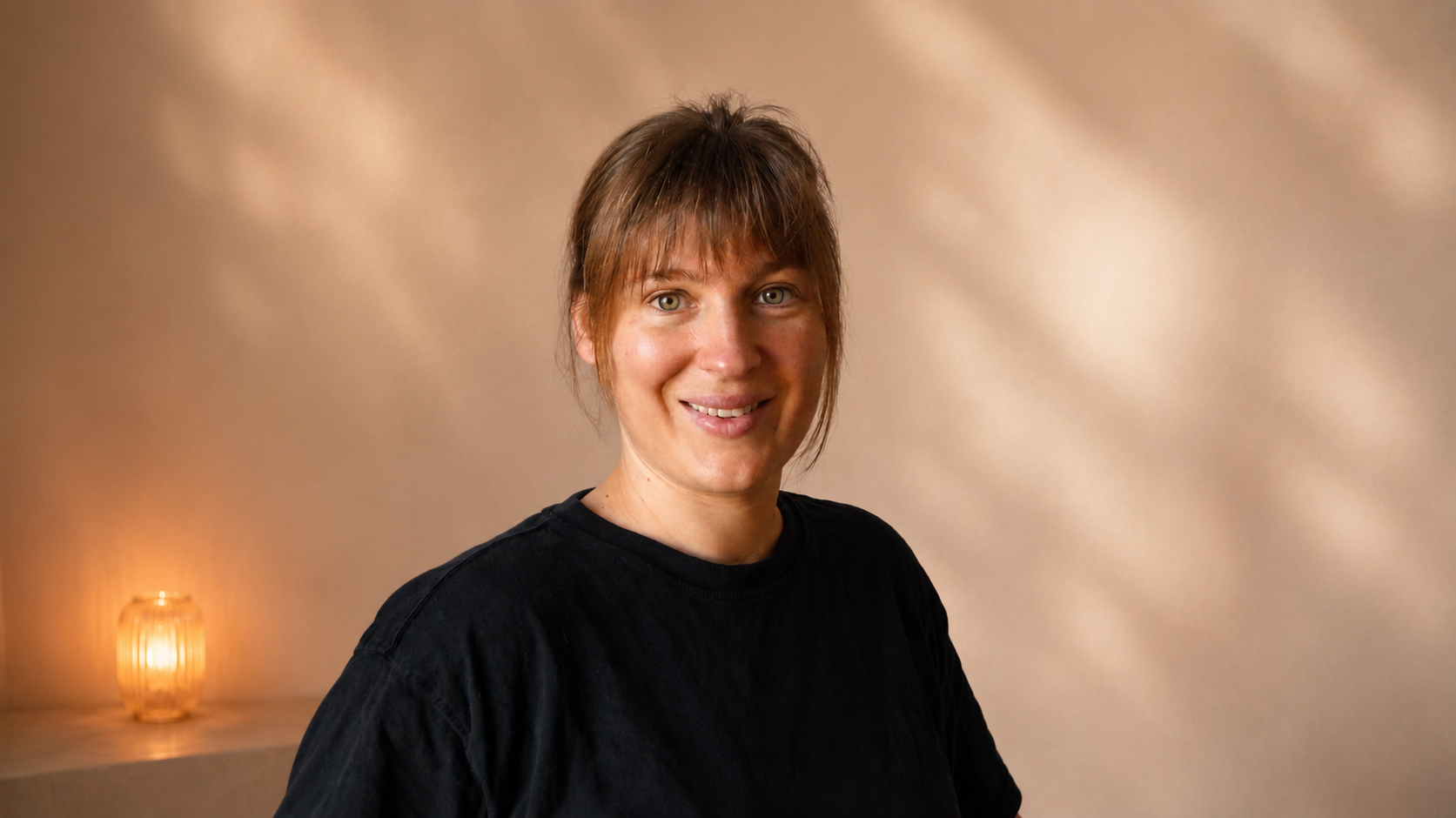 Portrait de Julie: une femme avec des cheveux blonds, souriante, portant un t-shirt noir, dans un décor intérieur avec une lumière douce.