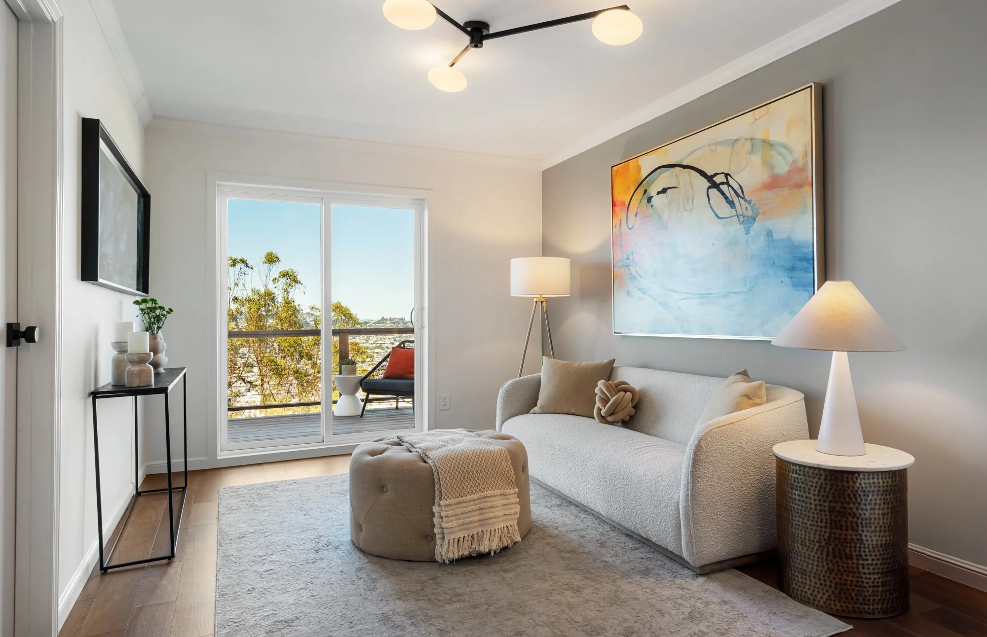 Modern living room with white sofa, abstract artwork on the wall, floor lamp, sliding glass door leading to balcony, and minimalist decor.
