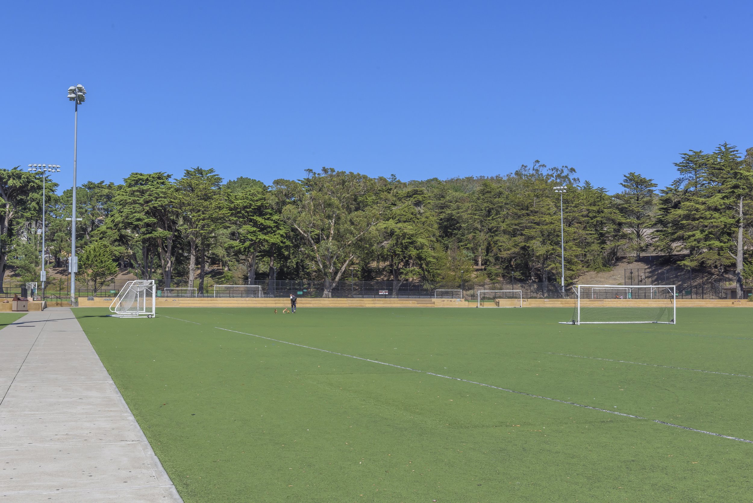 Empty soccer field with goalposts, trees in the background, and a clear blue sky.