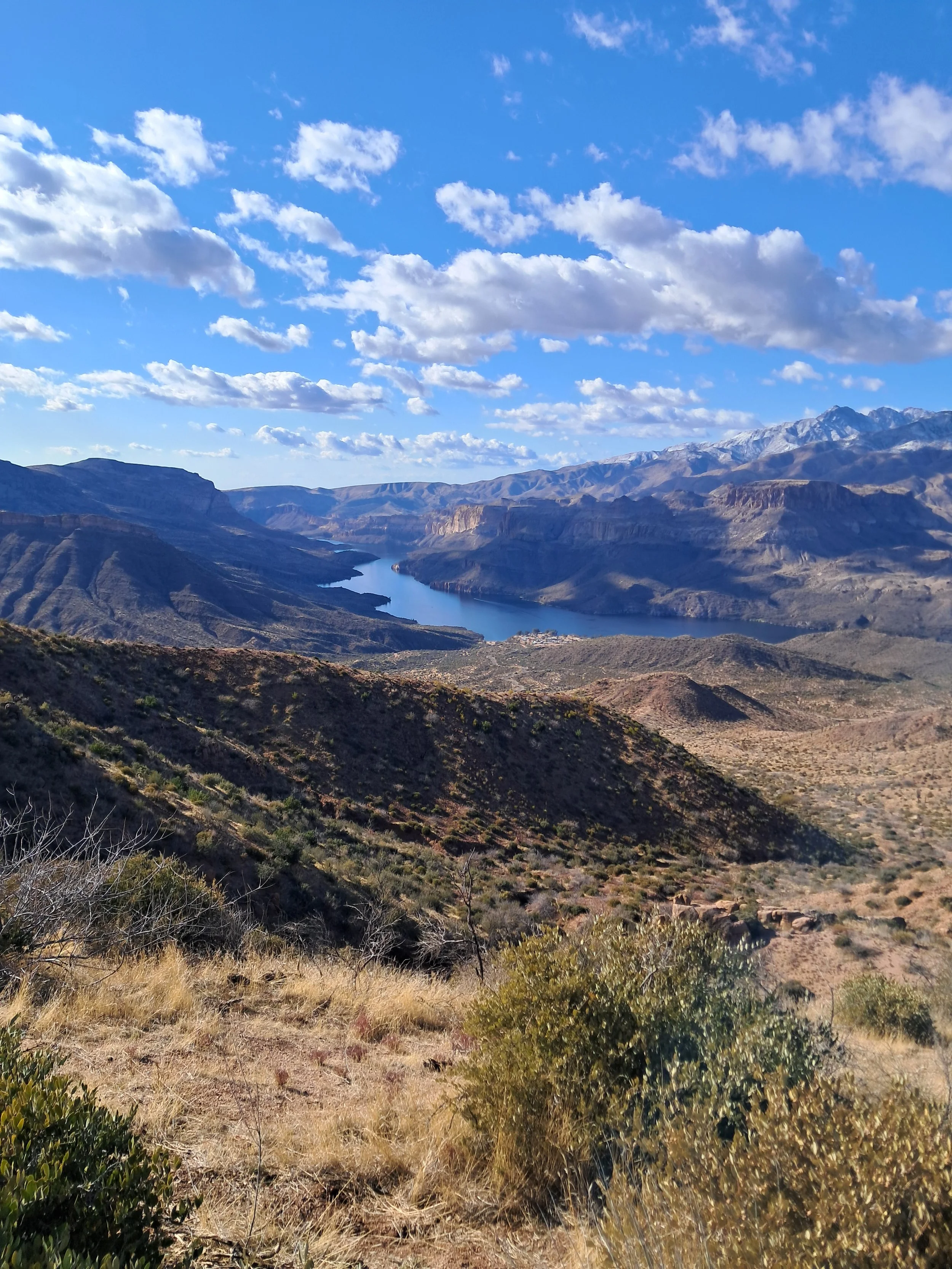 A scenic view of a river winding through a mountainous landscape with a blue sky and scattered white clouds.