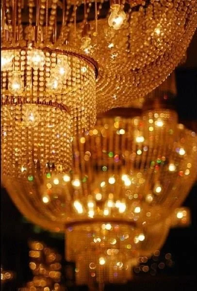 Close-up of multiple ornate, gold chandeliers with hanging crystals and glowing lights.