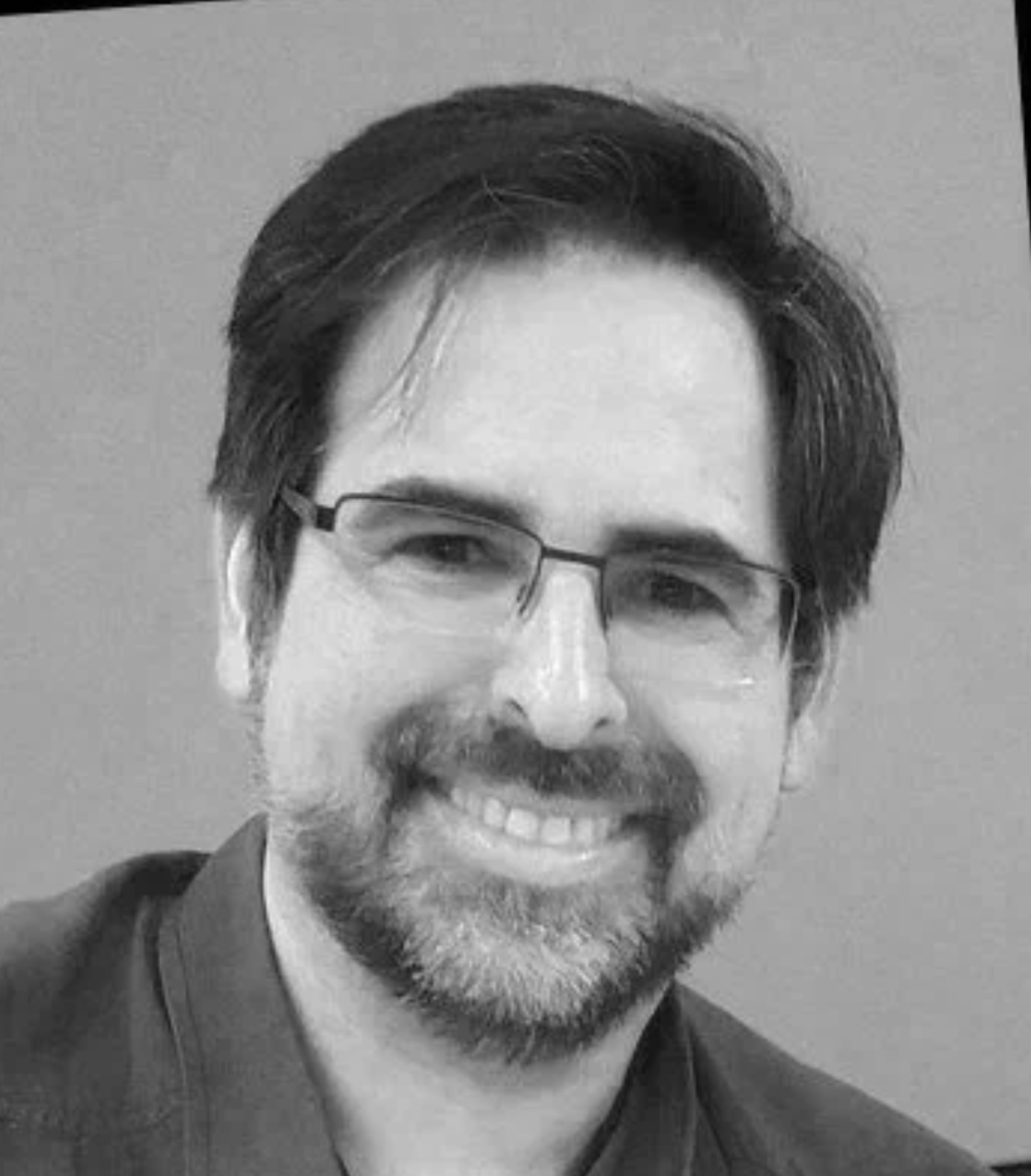 Black and white photo of a smiling man with glasses, a beard, and slightly wavy hair.