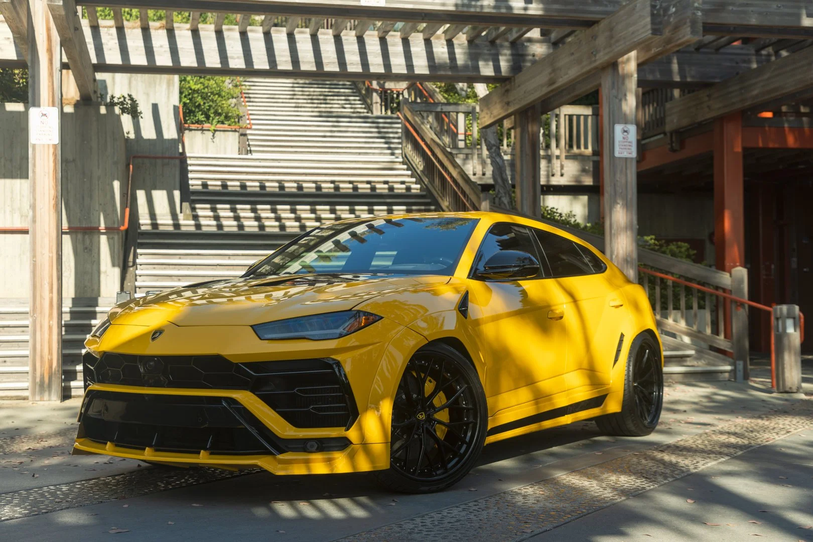 A yellow Lamborghini sports car parked outdoors near wooden stairs and a multi-level wooden parking structure.