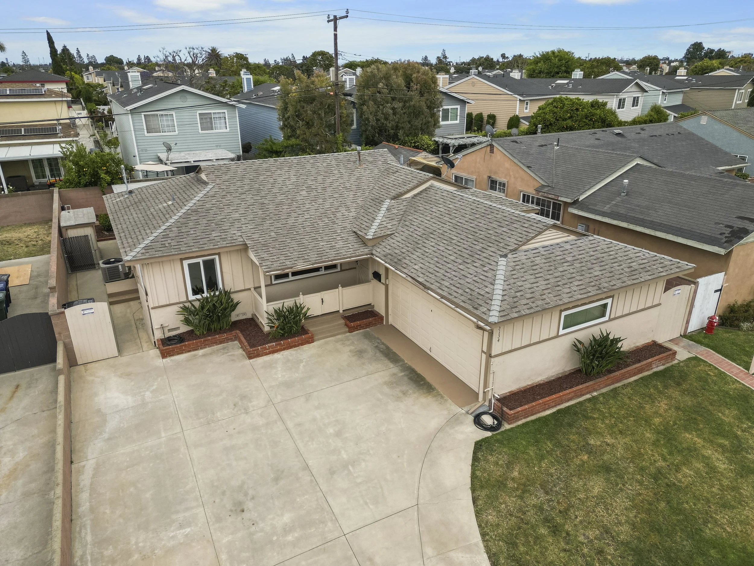 An aerial view of a suburban house with a concrete driveway, small front yard with grass, and neighboring houses in the background.