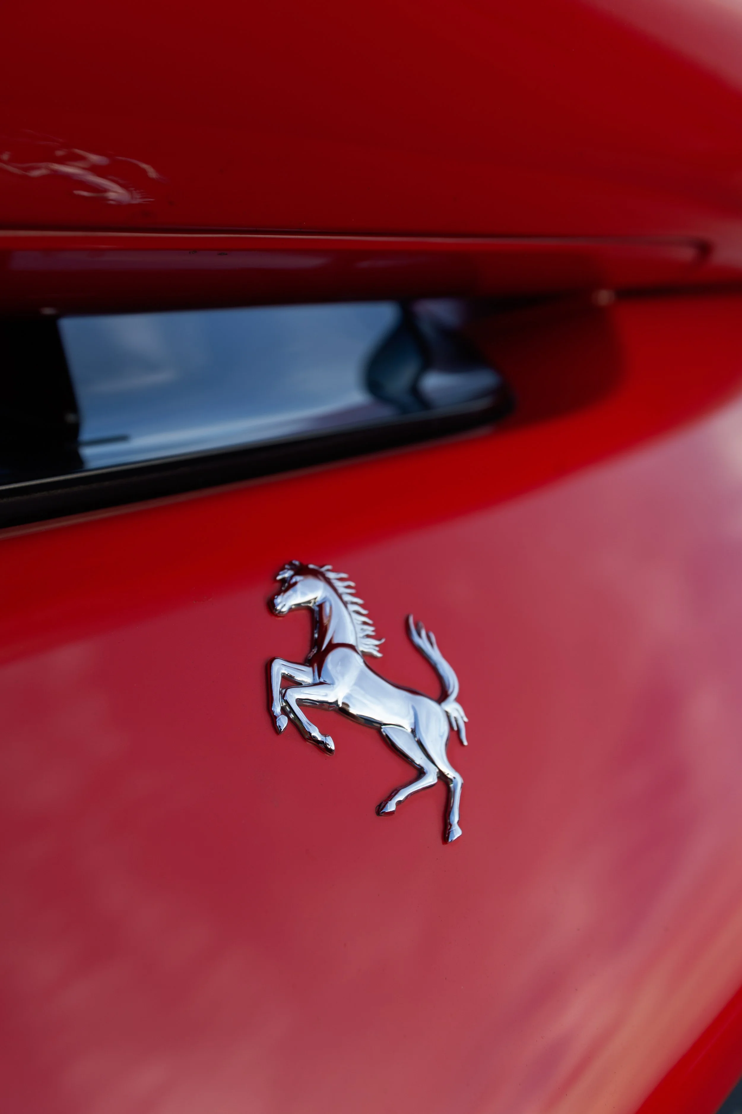 Close-up of a silver prancing horse emblem on a red Ferrari car.