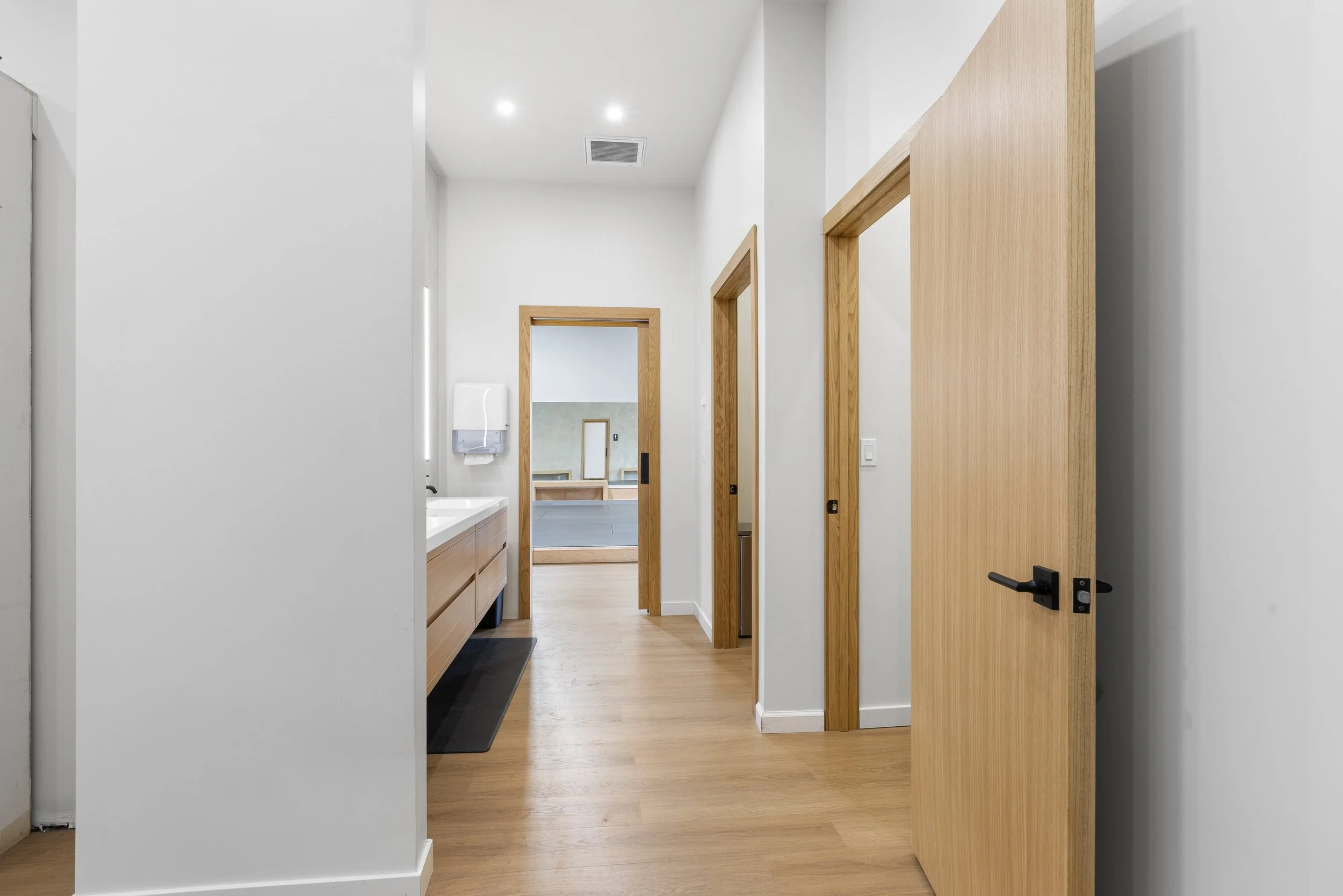 Inside view of a modern hallway with wooden doors, a sink area, and a mirror in a room at the end.