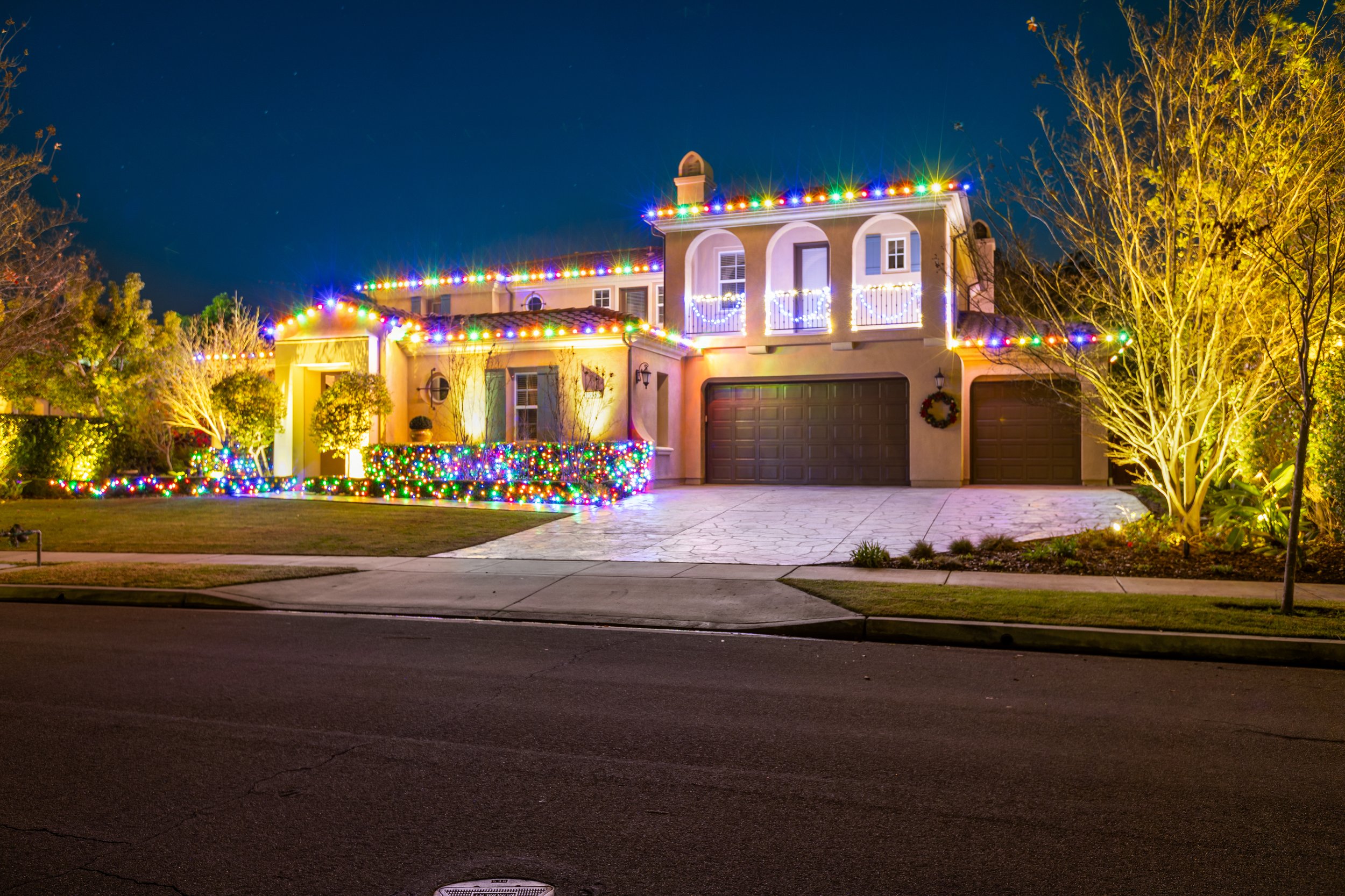 A house decorated with colorful Christmas lights at night, with a dark sky and trees around.