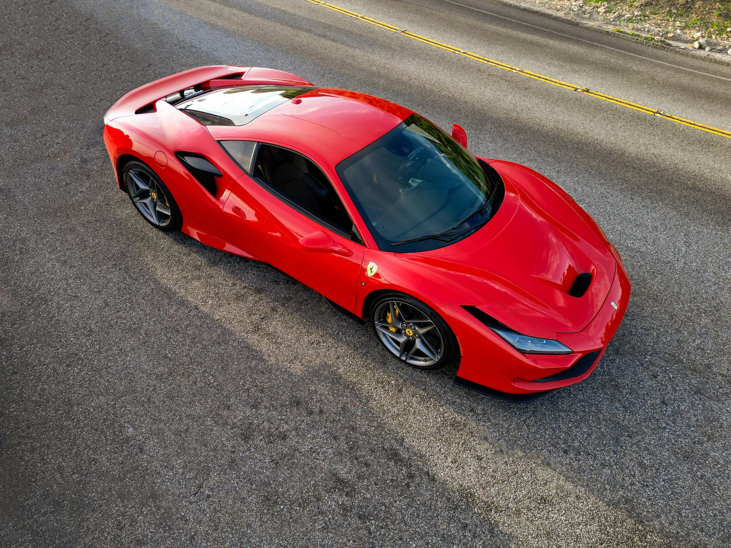 A red Ferrari sports car parked on the side of a two-lane road viewed from above.