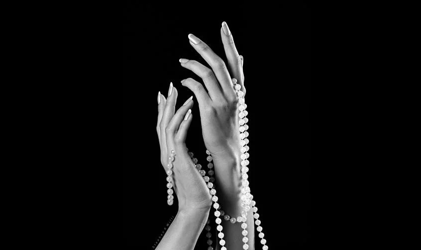 Black and white photo of two hands holding pearls against a black background.