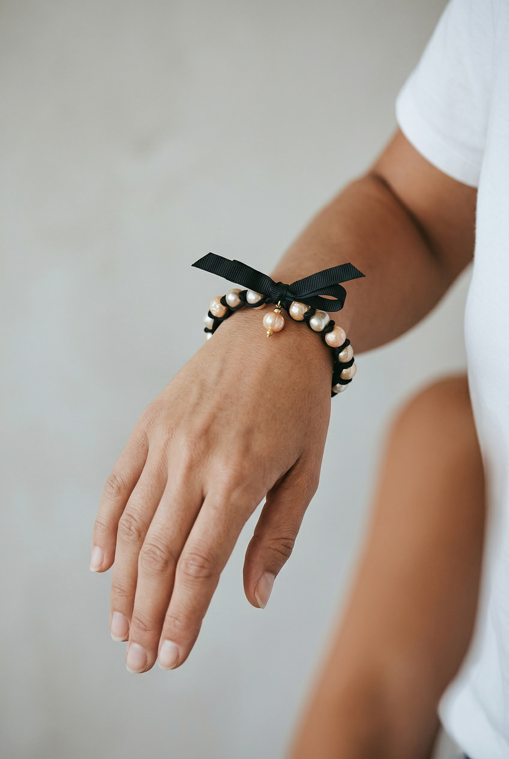 Close-up of a person's wrist adorned with a pearl bracelet featuring a black ribbon bow.
