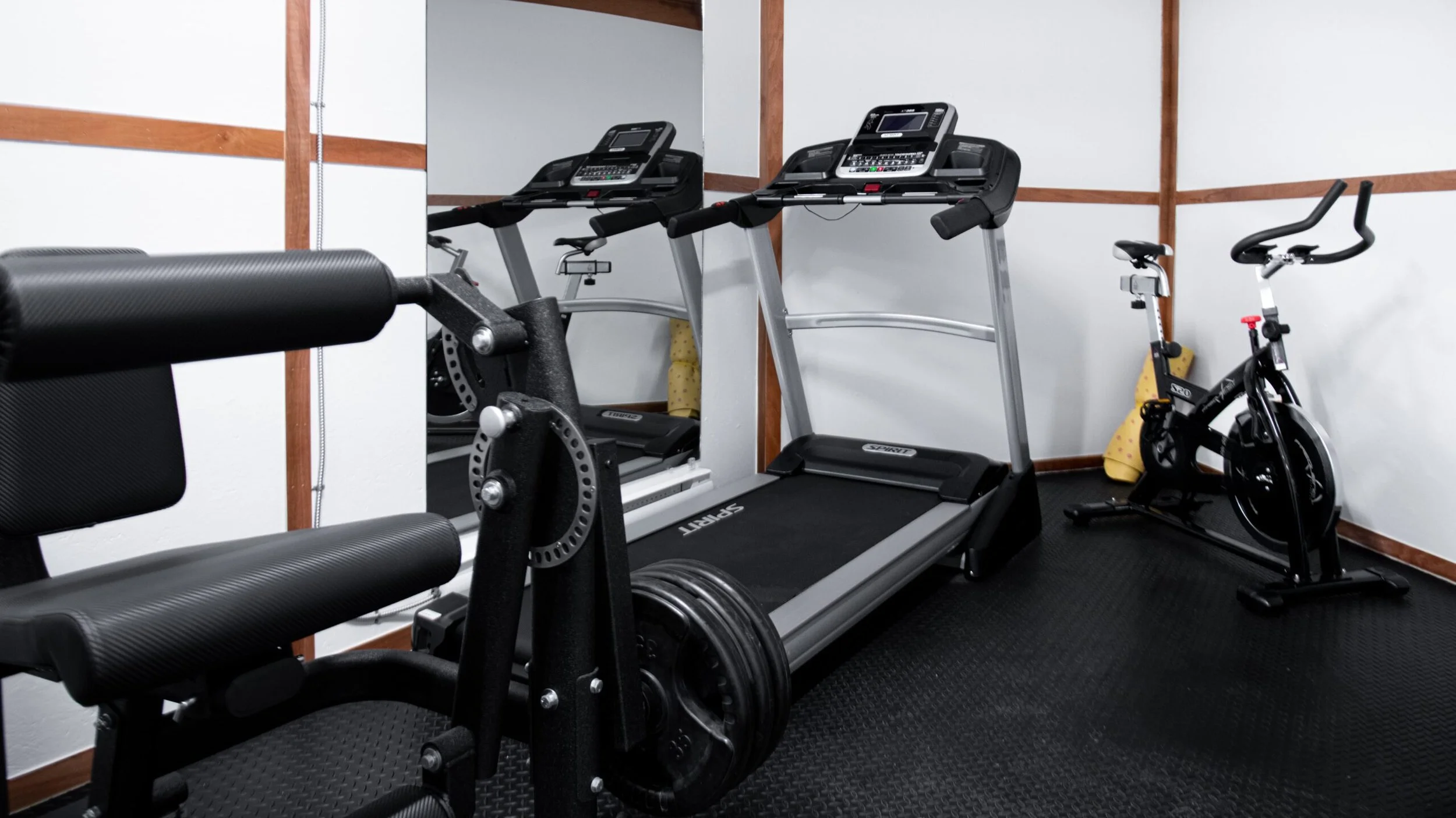 A small gym room with a treadmill, an exercise bike, and a weight bench.