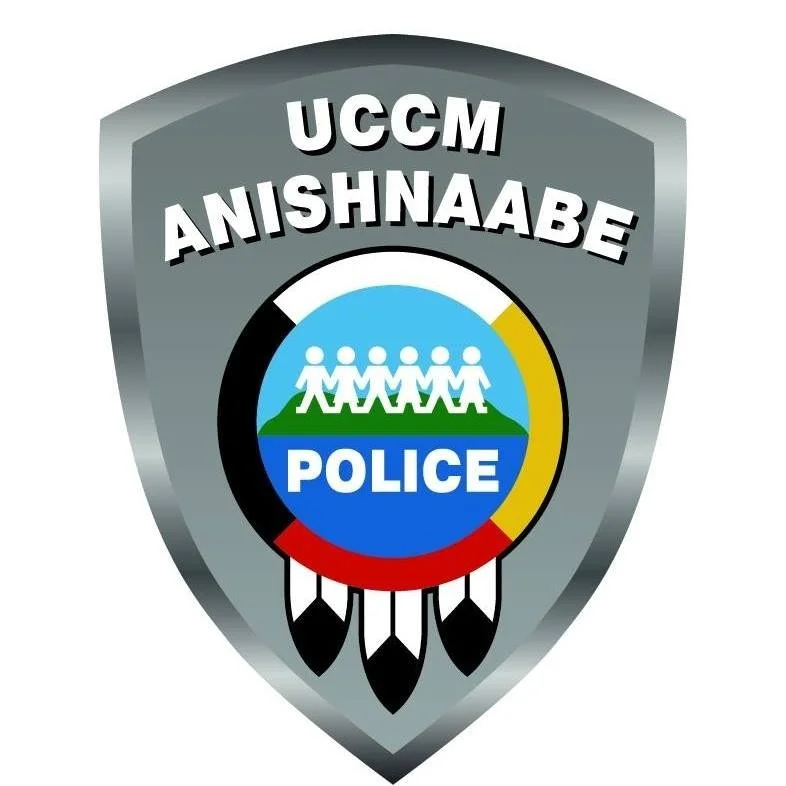Police badge with the words 'UCGM Anishnaabe' and images of people, a lake, and feathers.