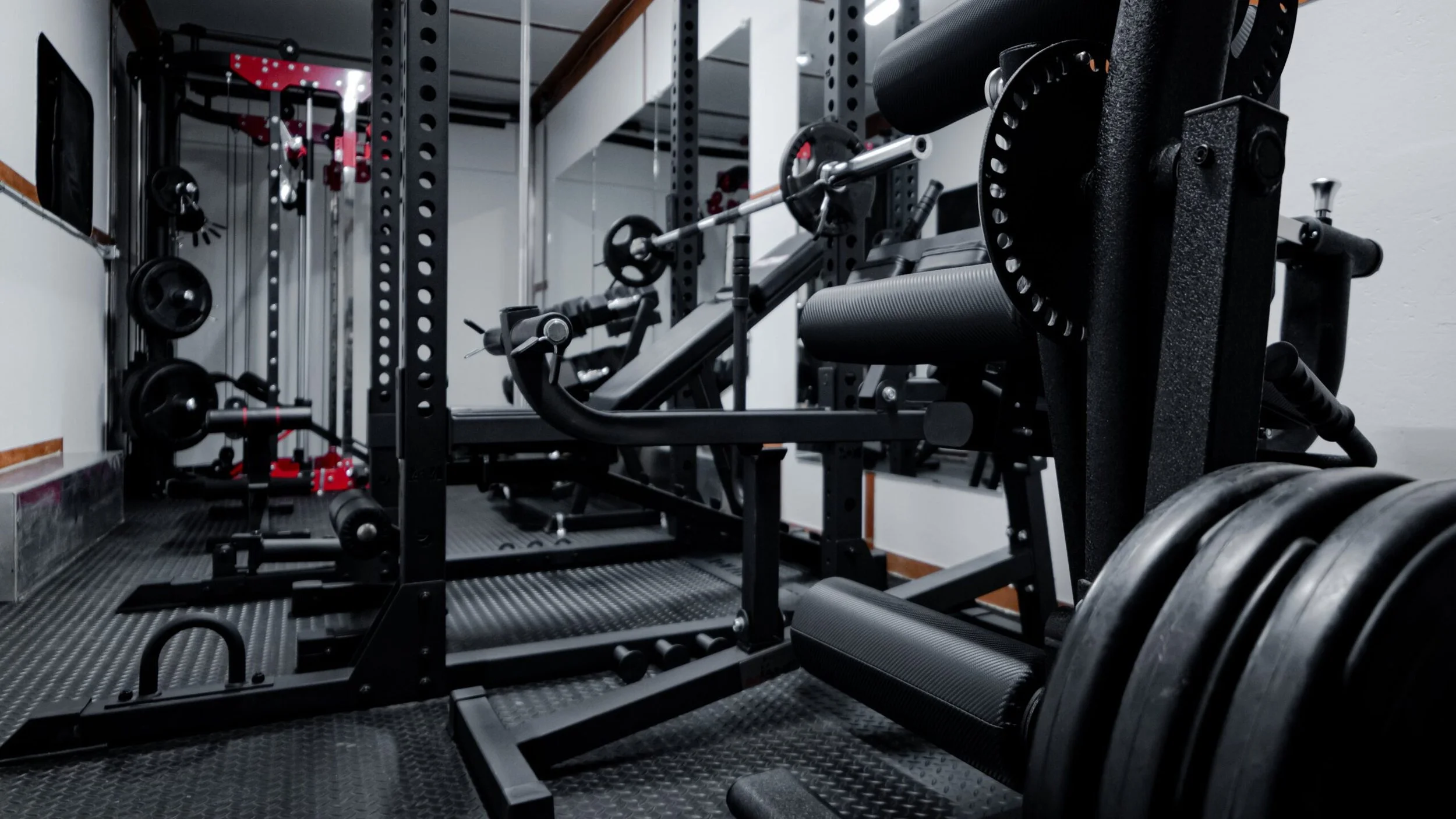 Empty home gym with weightlifting equipment including a bench press, barbell, weight plates, and resistance bands.