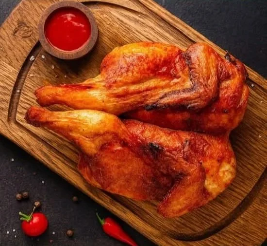 Two roasted chicken leg quarters on a wooden serving board with a small bowl of ketchup and some cherry tomatoes and a chili pepper on the side.