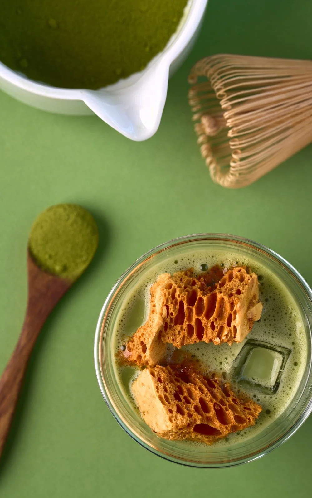 Two cups of matcha flavored dessert with creamy layers and green labels reading 'Premium Matcha Café Maiko' on a white surface with a green leafy plant in the background.