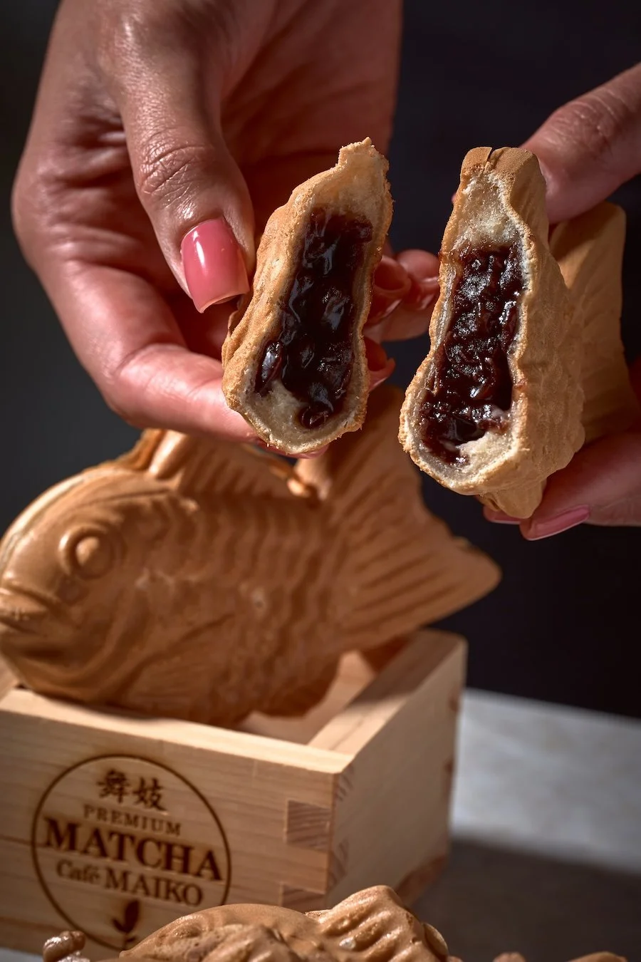 Person holding a halved taiyaki fish-shaped pastry filled with dark red bean paste at Matcha Cafe Maiko.