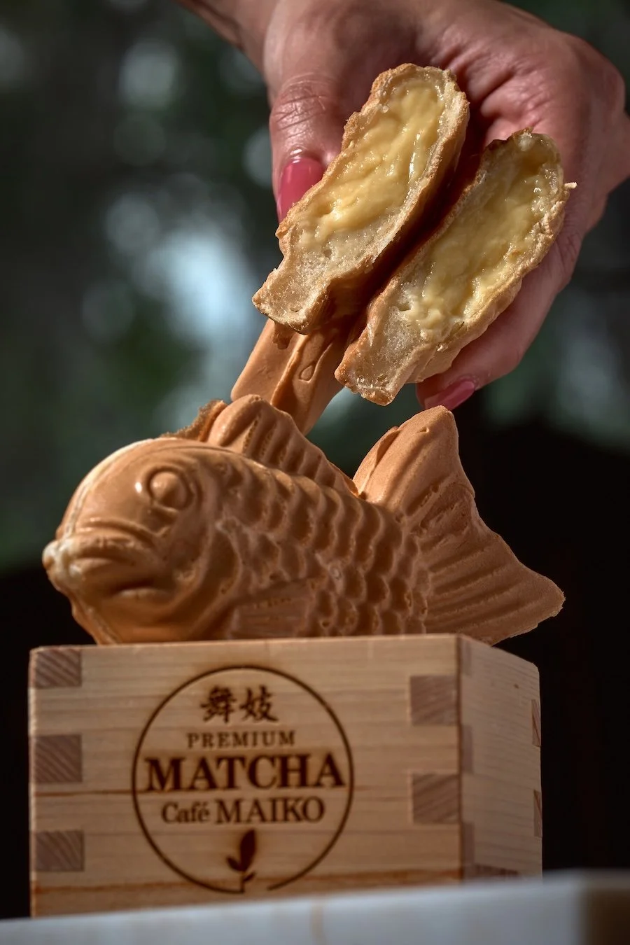 Person holding a halved taiyaki fish-shaped pastry filled with cheese at Matcha Cafe Maiko.