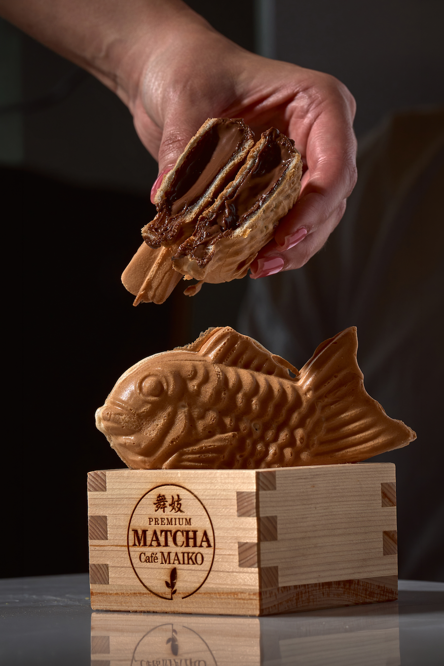 Close-up of Nutella Taiyaki, displayed on a table. One Taiyaki is in a wooden box with Japanese characters and text reading "Premium Matcha Cafe Maiko."
