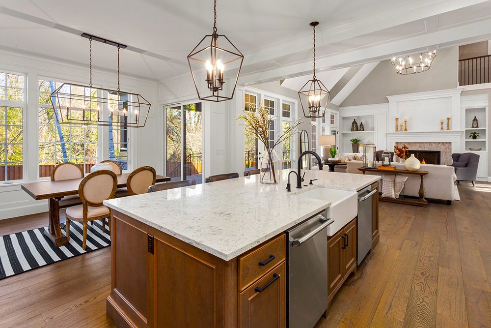 Open-concept kitchen and living room with large windows, white cabinetry, and modern lighting fixtures.