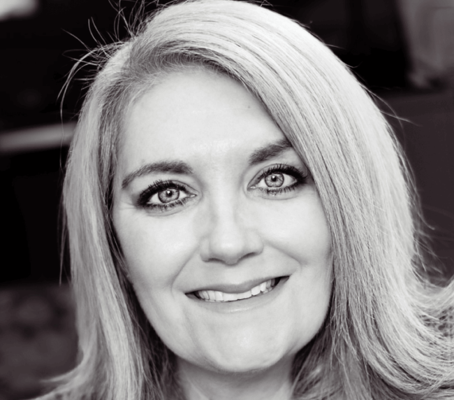 Black and white photo of a smiling woman with light-colored hair and bright eyes.