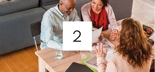 Three people sitting at a table during a meeting, with papers and a glass of water.