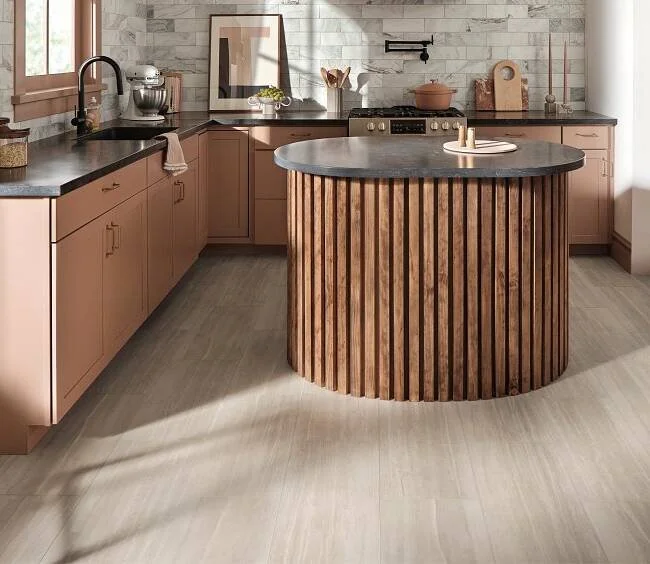 Modern kitchen with pink cabinets, black countertops, a round wooden island with vertical slats, and a gray marble countertop.
