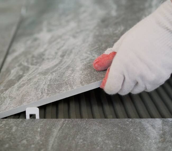 A person wearing a white work glove with red accents is installing or adjusting a large, gray tiled surface, which is being fitted onto a black, textured surface.