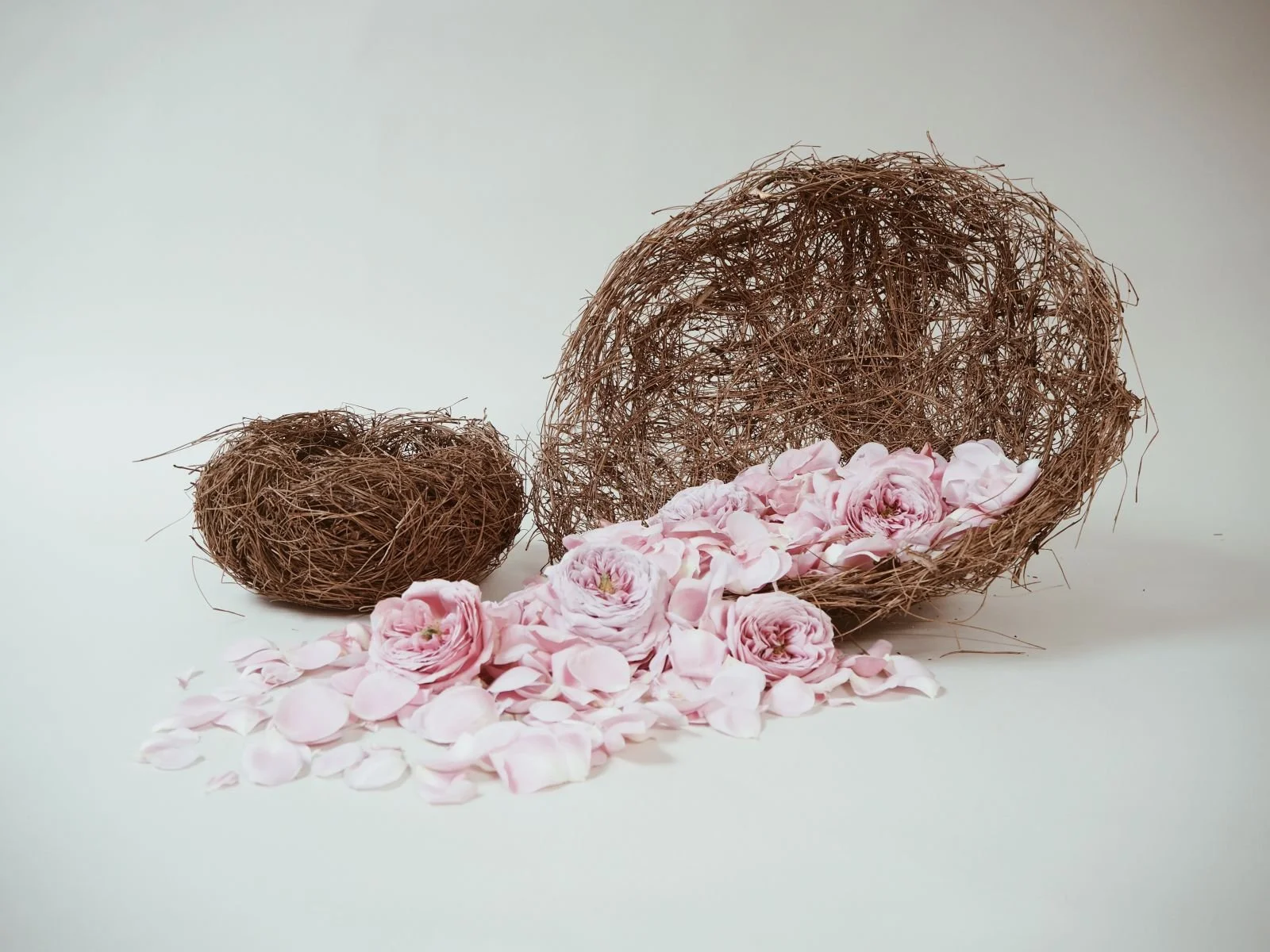Large Pine Needle Vessel by Kept LA tipped on its side with  pink rose petals spilling out, showing use as a flower girl  basket for weddings alongside small size vessel