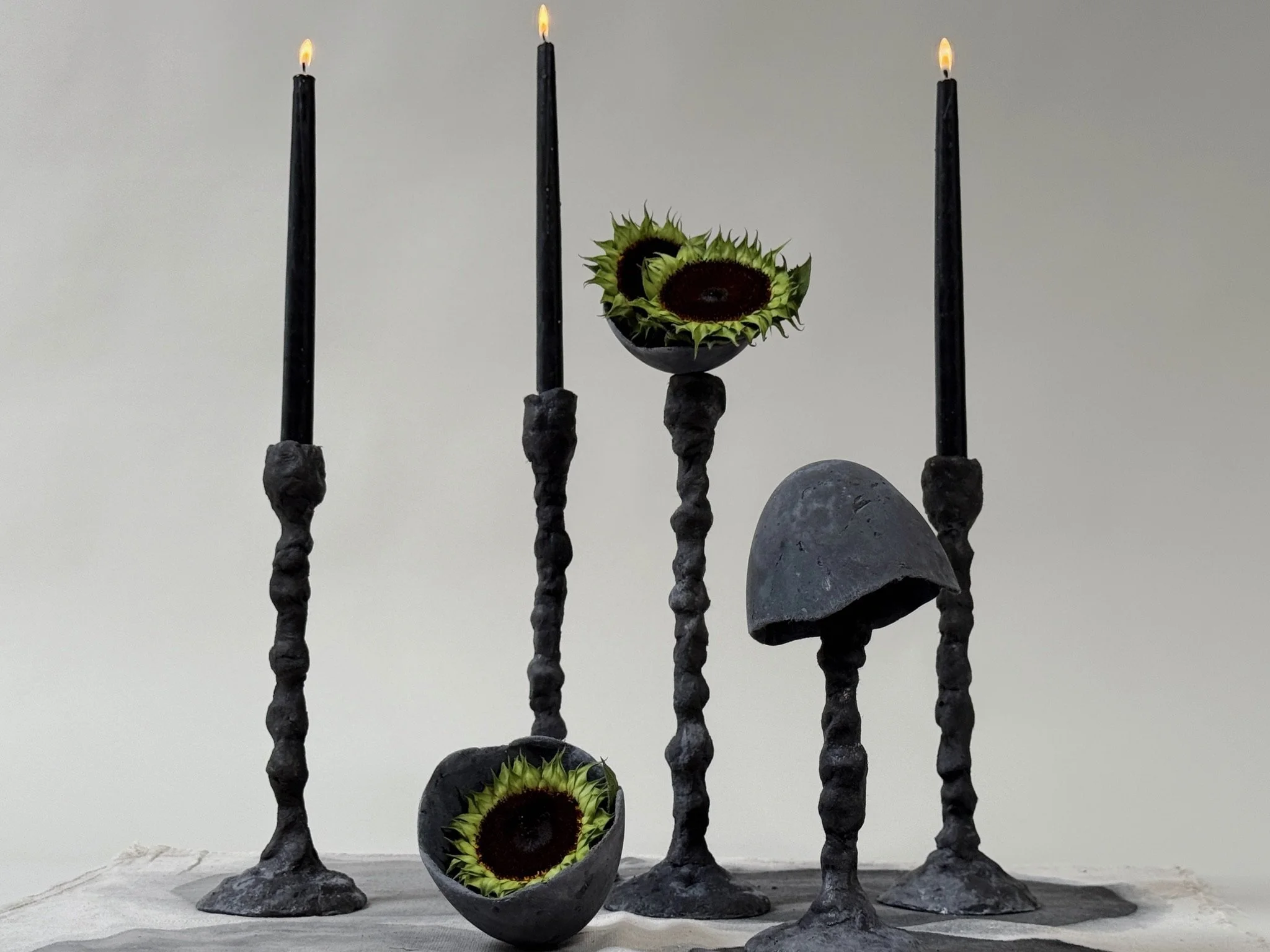 Alberto Candlestick set of three by Kept LA in black concrete  with lit taper candles, Little Cup inserts holding sunflower heads  and a volcanic lava stone candlestick, full styled composition