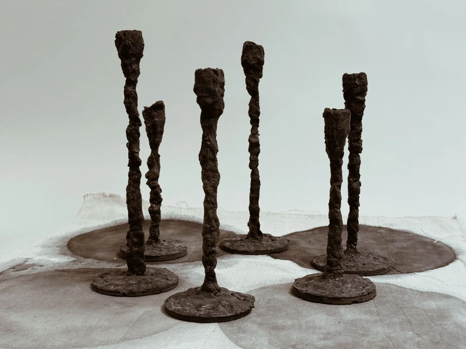 Group of Alberto Candlesticks by Kept LA in varied heights shown  on concrete disc bases in studio setting, demonstrating range of  scale and Giacometti-inspired elongated forms