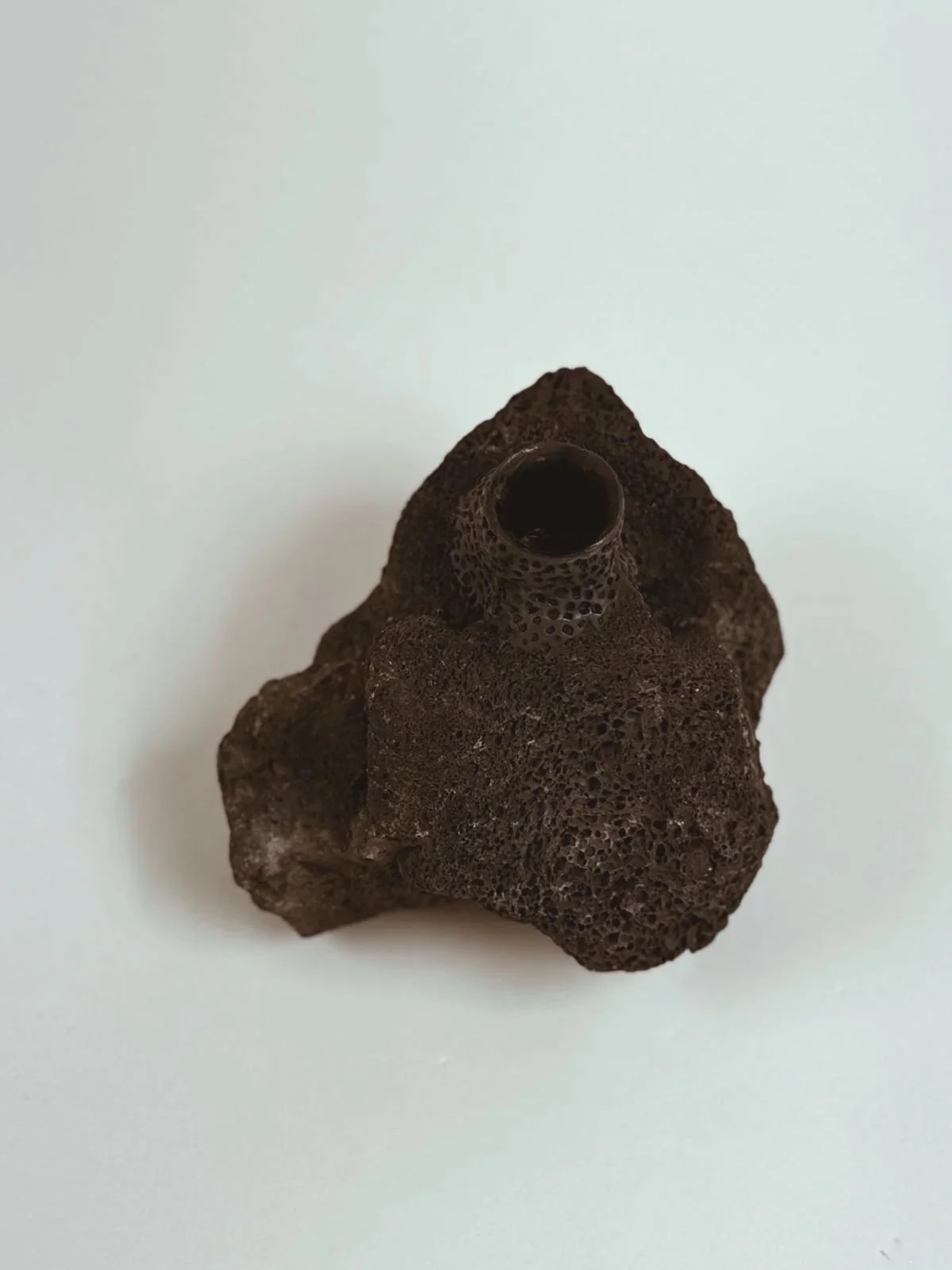 Angled top view of Volcanic Candlestick by Kept LA showing  taper candle opening in lava stone surface with raw industrial  clay and steel construction detail