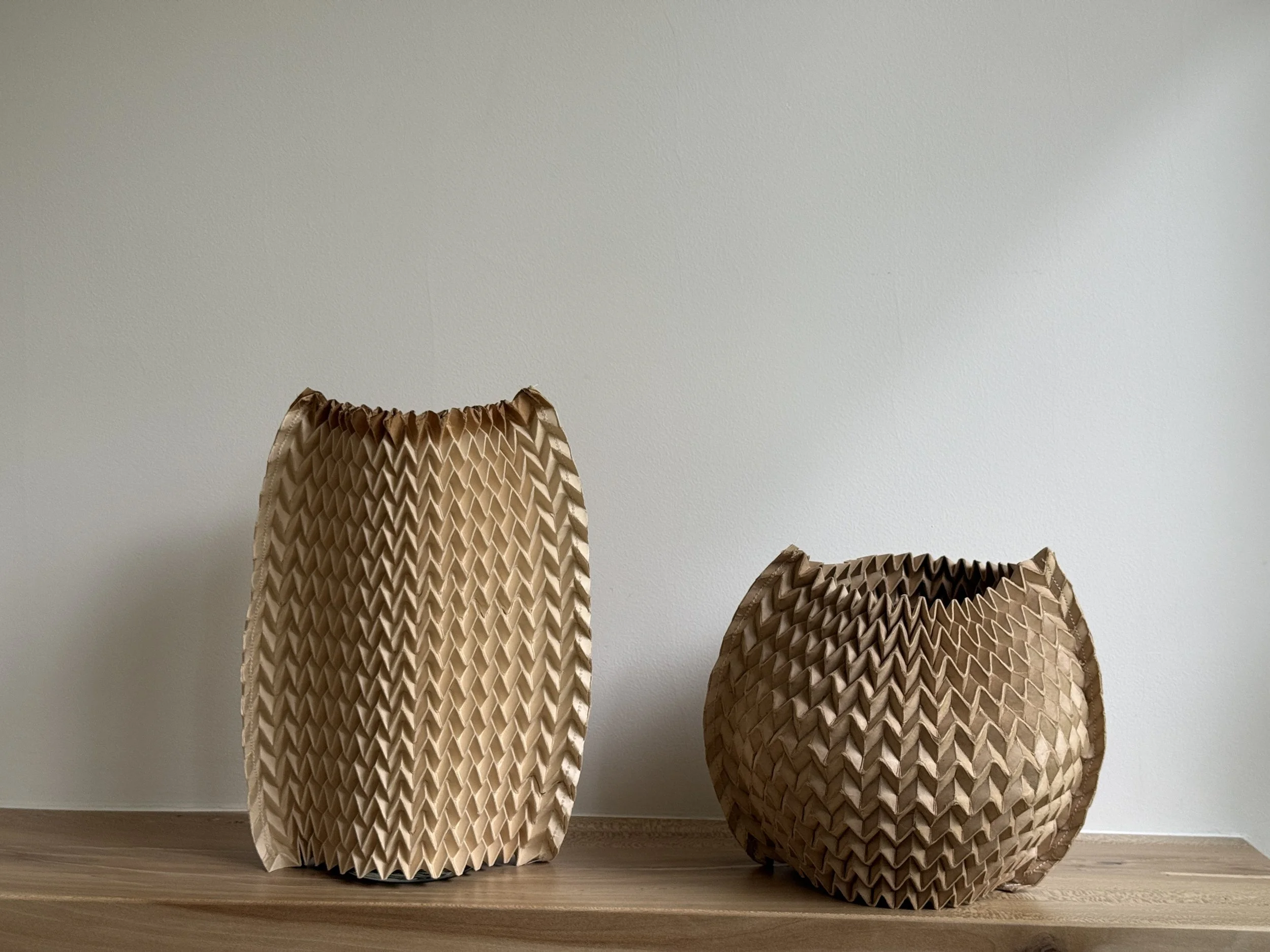 Two Pleated Paper Vase Sleeves by Kept LA on wooden shelf —  medium cylinder and small bubble sizes showing worn textural  quality of retired fashion industry pleating forms