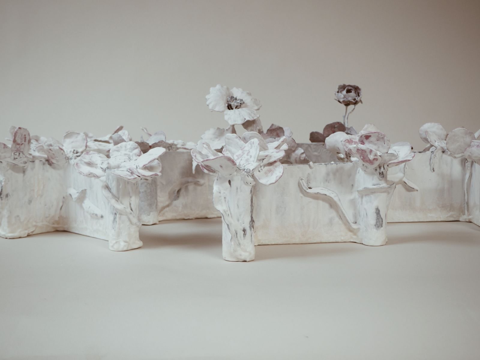 Close view of Tole Candelabra Vessels by Kept LA styled with dried  roses and wax flower vessels showing bone-white glaze with pink and  lavender undertones on found metal forms