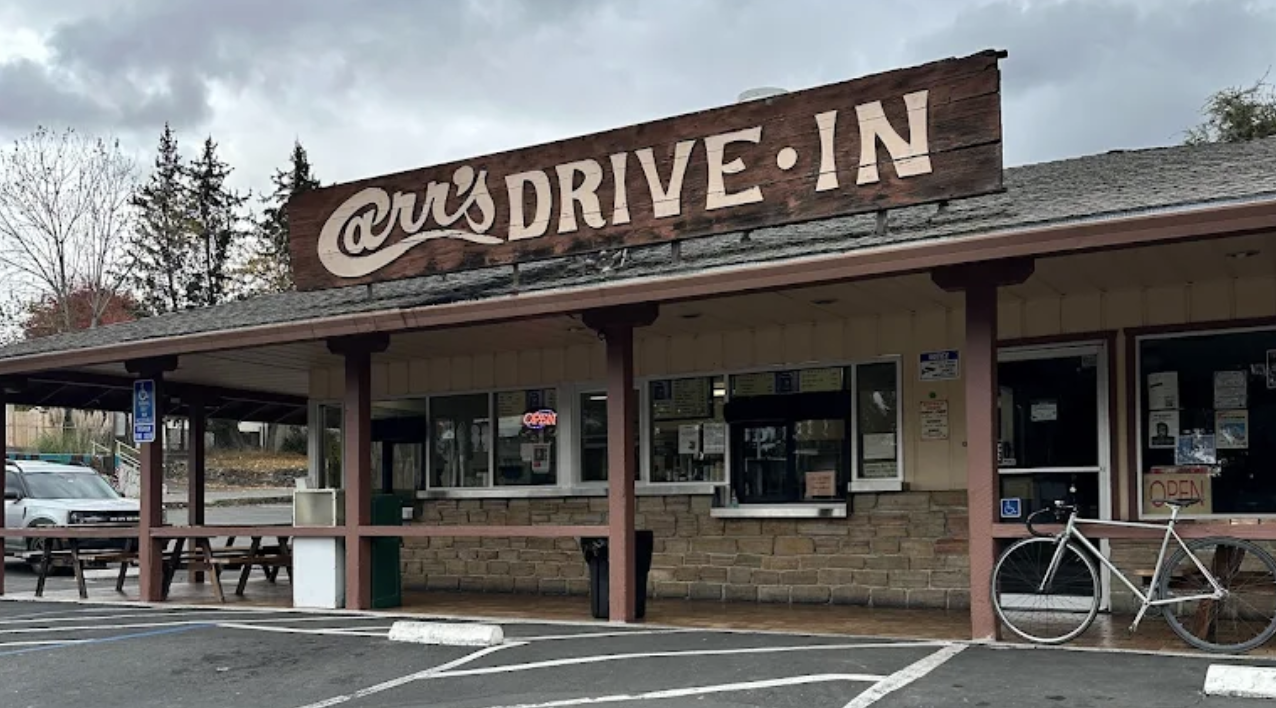 Exterior of Art's Drive-In diner with a wooden sign, parking lot, bicycle, and overcast sky.
