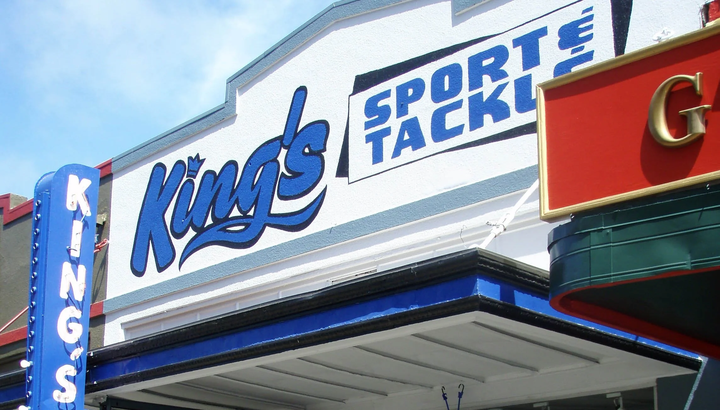 Sign for King's Sport and Tackle with blue and white lettering on a building, with a partial view of a red marquee and a vertical blue sign that says 'KING'S' in white letters.