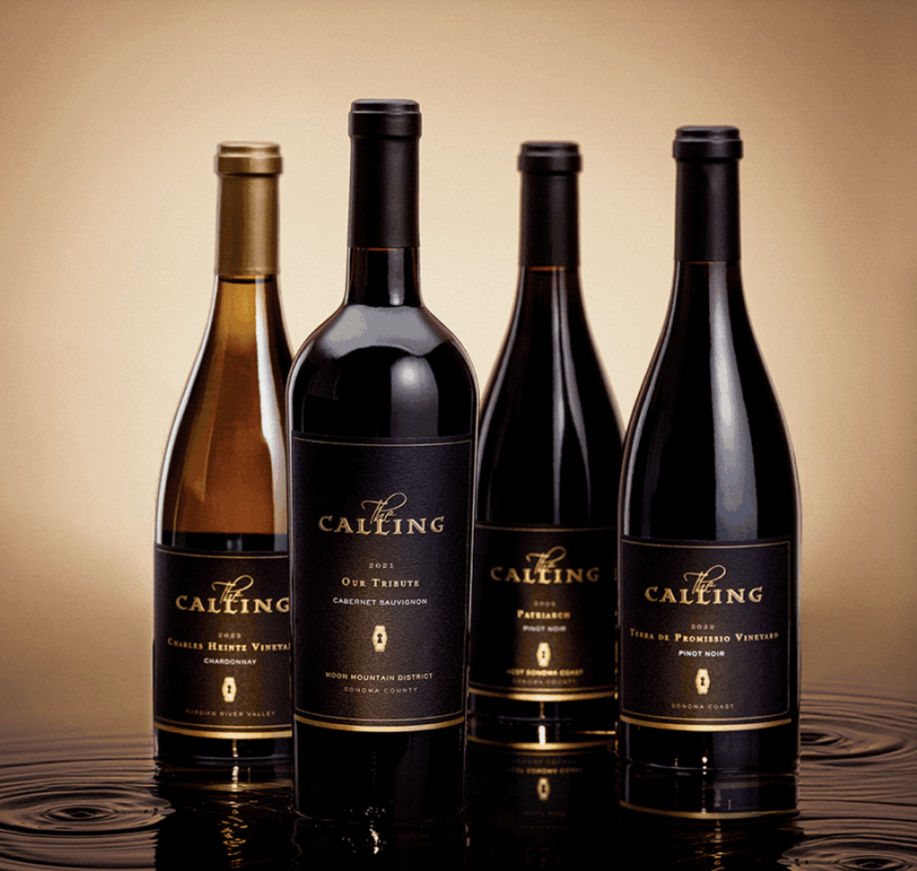 Four bottles of wine with black labels and gold text, standing on a reflective surface, with a beige background.