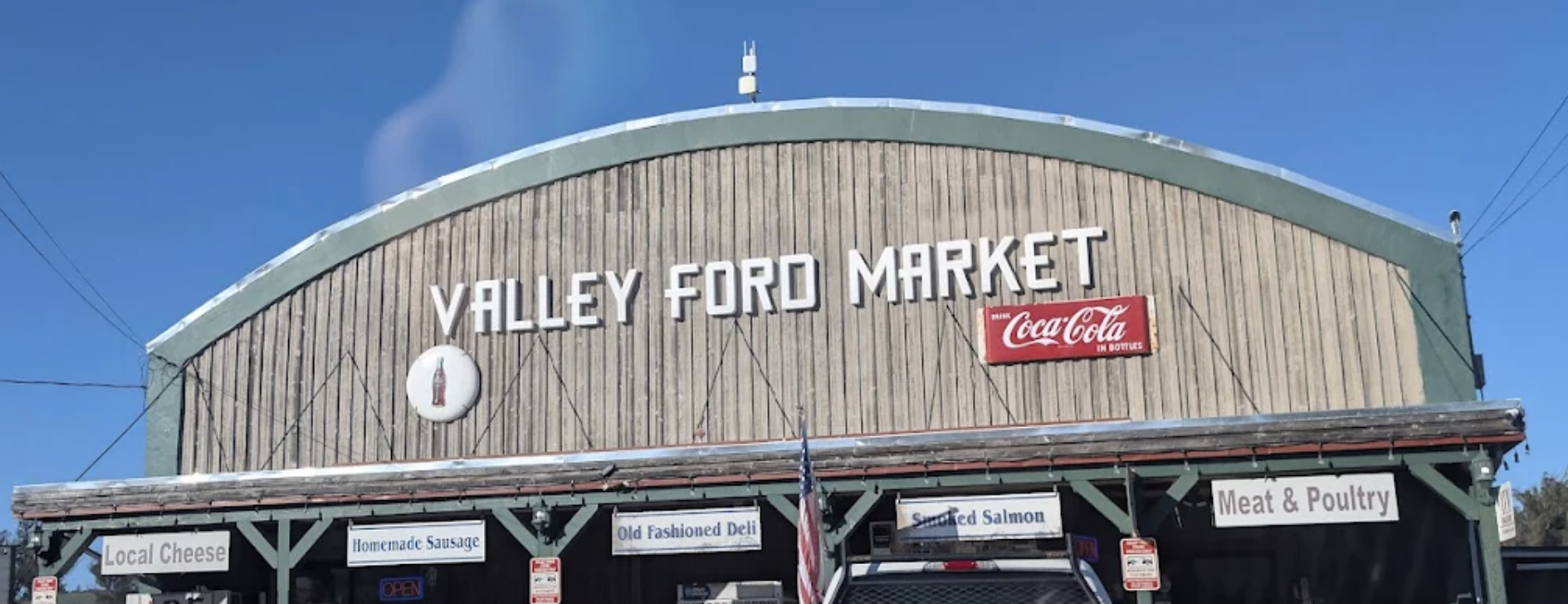 The exterior of Valley Ford Market building with a sign and advertisement for Coca-Cola, under a clear blue sky.