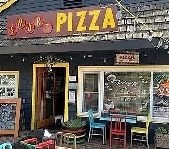 Exterior of a pizza restaurant named Smart Pizza with colorful chairs outside
