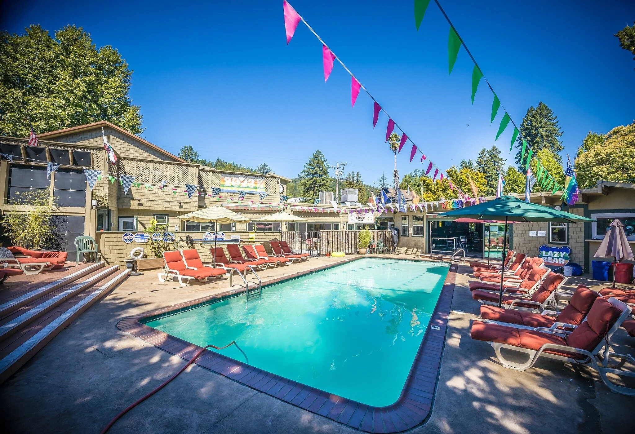Outdoor pool surrounded by lounge chairs, umbrellas, and colorful decorations on a sunny day.