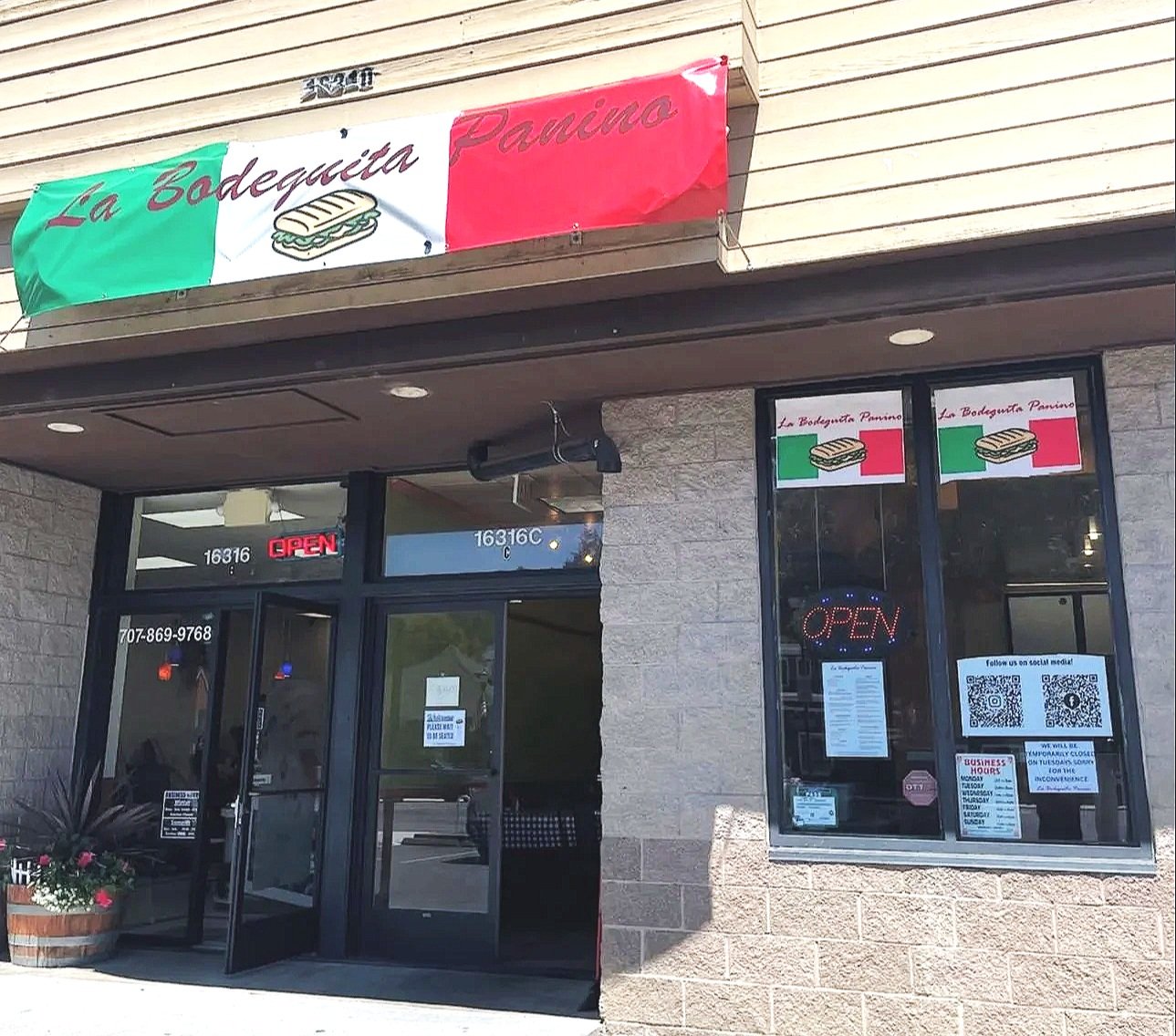 Front view of a restaurant called La Bodeguita Panino, with signs in Italian colors and a sandwich illustration, displaying open signs and operational hours.
