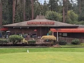 Exterior view of Northwood Restaurant with a wooden building, red signage, and outdoor patio, surrounded by trees.