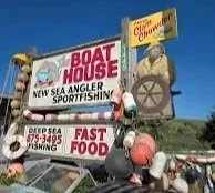 Billboard advertising Boat House, a New Eagle Sportfishing business, with signs for deep sea fishing, fast food, and a Clam Chowder ad, featuring a man in a yellow shirt and glasses.