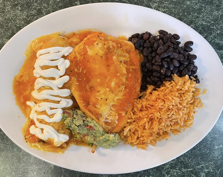 Plate of Mexican food with grilled chicken topped with melted cheese and sour cream, a side of black beans, Mexican rice, and mashed avocado with tomatoes.