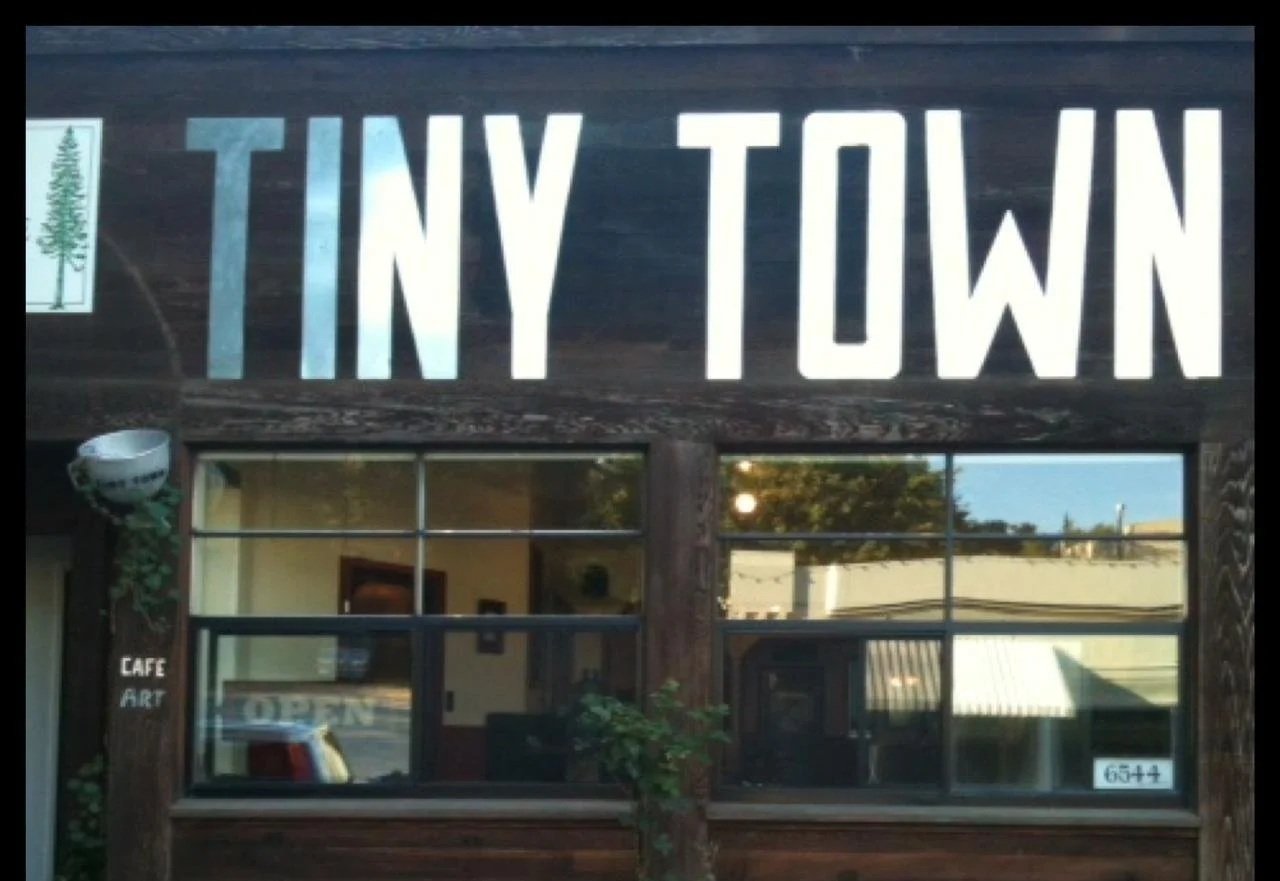 A storefront with a sign that reads 'Tiny Town' in large white letters on a dark wooden background.